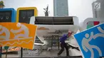 Pekerja melintas dibawah papan sosialisasi Asian Games 2018 terlihat roboh akibat hujan angin di Bundaran HI, Jakarta, Senin (11/9). (Liputan6.com/Faizal Fanani)