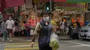 Seorang perempuan mengenakan masker wajah membawa produk di seberang jalan di Hong Kong, Minggu (13/3/2022). Pemimpin Hong Kong Carrie Lam mengatakan infeksi Covid-19 di kota itu belum melewati puncaknya meskipun jumlah kasus harian baru-baru ini sedikit menurun. (AP Photo/Kin Cheung)