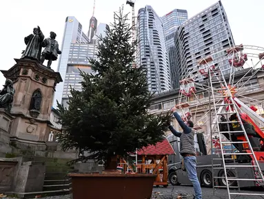 Seorang pria menghias pohon Natal di depan gedung pencakar langit salah satu distrik perbankan di pusat kota Frankfurt am Main, Jerman, pada tanggal 21 November 2024. (Kirill KUDRYAVTSEV/AFP)