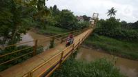 Pengendara motor melintasi jembatan gantung Kuning yang menghubungkan Pasar Minggu Poltangan ke Cililitan Condet, Jakarta, Selasa (28/12/2021). Jembatan gantung dengan panjang 40 meter di atas sungai Ciliwung tersebut baru baru ini dijadikan lokasi foto untuk konten medsos. (merdeka.com/Imam Buhori)