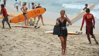 Turis berjalan di pantai Kuta di pulau pariwisata Indonesia di Bali (4/1). Pantai ini dilengkapi lahan parkir di sepanjang pantai, kamar mandi umum, payung pantai, kios makanan dan minuman, serta tempat penyewaan papan selancar. (AFP Photo/Sony Tunbelaka)