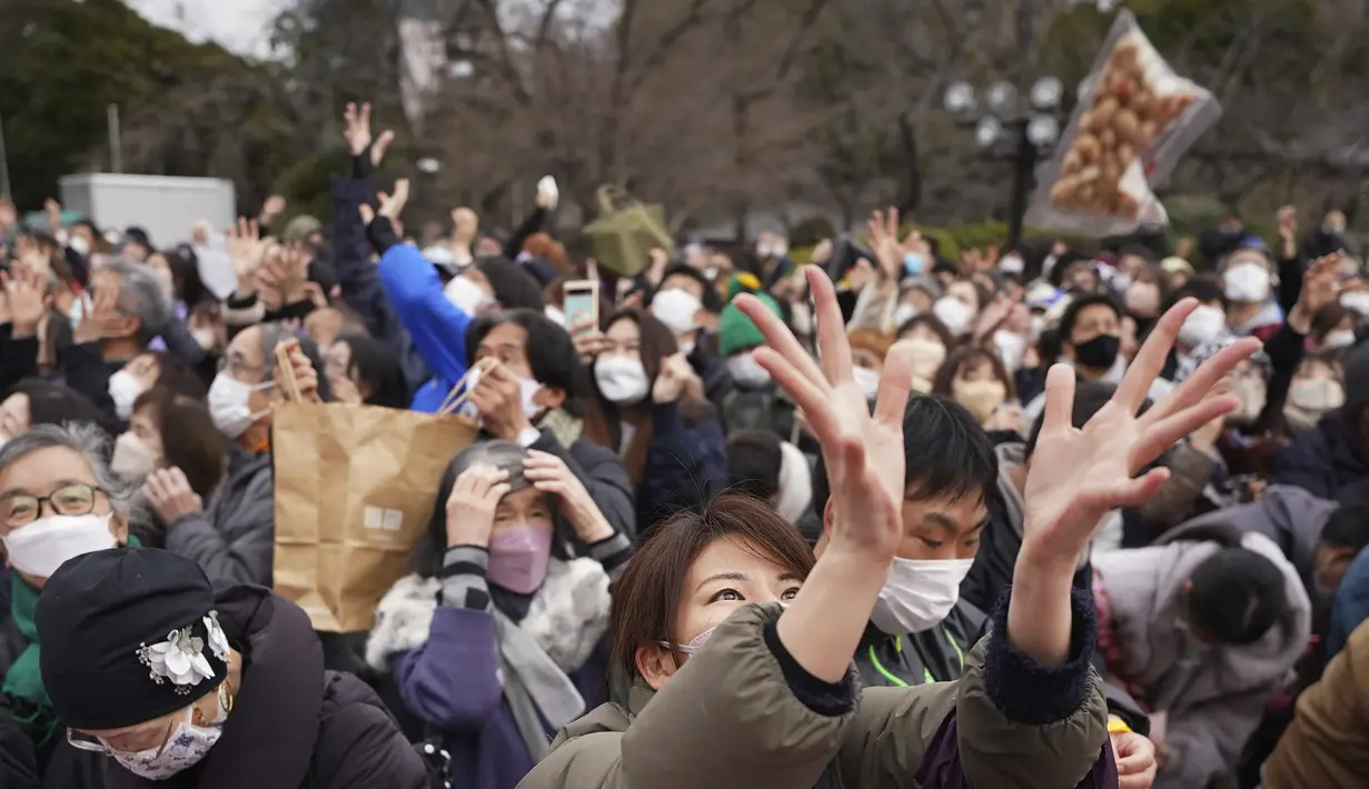 Orang-orang mencoba menangkap kacang keberuntungan yang disebarkan selama "Mame-maki", upacara melempar kacang, di kuil Buddha Zojoji, Tokyo, Jumat (3/2/2023). Ritual yang diyakini membawa keberuntungan dan mengusir kejahatan ini dilakukan setiap tahun untuk menandai awal musim semi dalam kalender lunar. (AP Photo/Eugene Hoshiko)