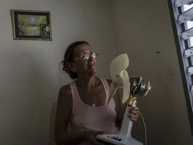 Miriam Cortes berpose dengan kipasnya di samping foto Fidel Castro saat pemadaman listrik pagi hari, di rumahnya di Regla, Kuba, Senin, 1 Agustus 2022. Pihak berwenang telah mengumumkan akan memulai pemadaman listrik terjadwal mulai awal Agustus. (AP Photo/Ramon Espinosa)