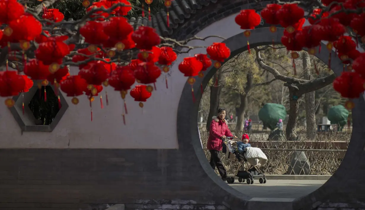 Seorang wanita membawa balita melihat lampion yang menggantung di pohon di taman Ditan di Beijing (1/2). Tahun Baru Imlek jatuh pada 16 Februari tahun ini, dengan perayaan yang berlangsung selama seminggu di China. (AFP Photo/Nicolas Asfouri)