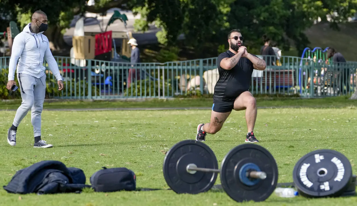 Seorang trainer menyaksikan anggota fitness berolahraga di sebuah taman di pinggiran timur Sydney, pada 14 September 2021. Pelatih pribadi telah mengubah taman kawasan tepi laut di Rushcutters Bay menjadi gym luar ruangan untuk menyiasati pembatasan lockdown karena pandemi covid-19. (AP/Mark Baker)