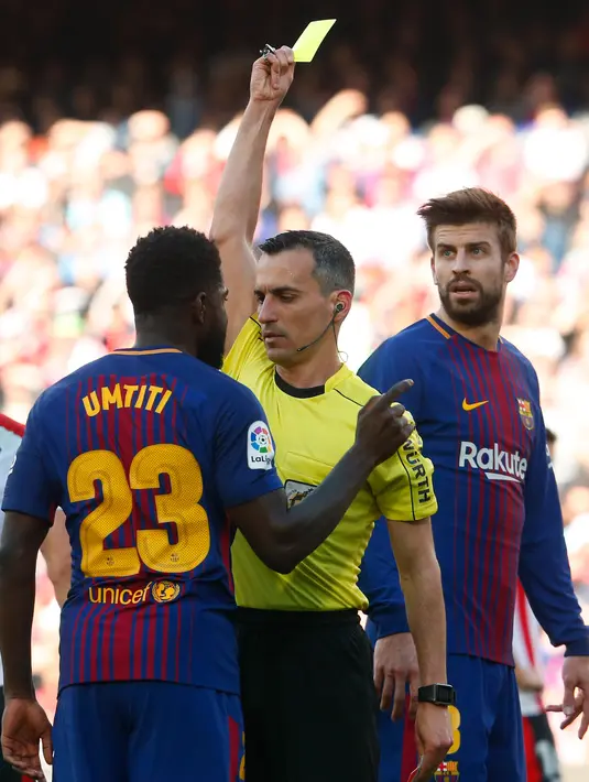 Wasit memberikan kartu kuning kepada bek Prancis Barcelona Samuel Umtiti saat melawan Athletic Bilbao dalam pertandingan La Liga Spanyol di stadion Camp Nou di Barcelona (18/3). (AFP Photo/Pau Barrena)