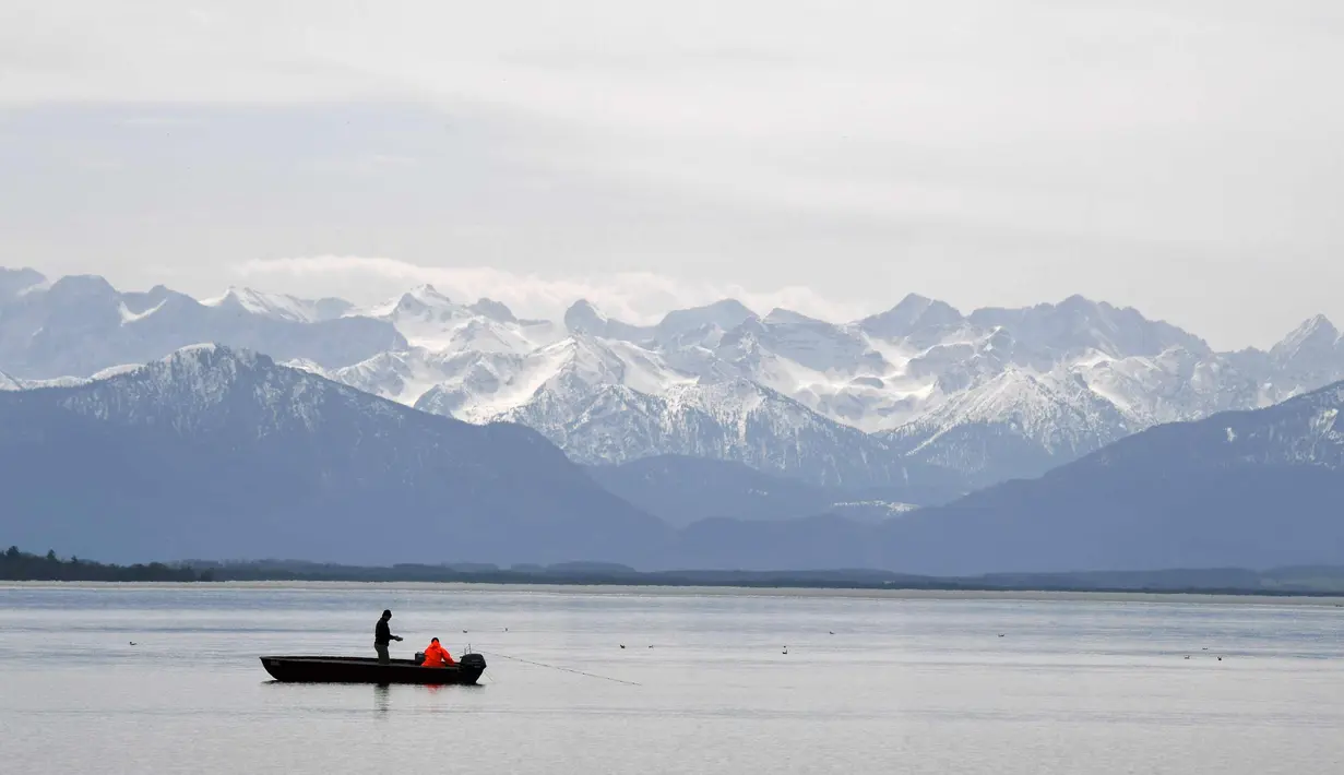 Nelayan menangkap ikan di depan pegunungan Alp di danau Starnberger See dekat desa Starnberg, Jerman selatan, selama cuaca musim semi yang bagus dengan suhu 15 derajat pada 3 April 2018. (AFP Photo/Christof Stache)