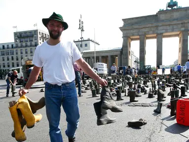 Seorang peternak sapi perah menyebarkan sepatu boots selama aksi protes di depan gerbang Brandenburg, Berlin, Jerman, Senin (30/5).  Mereka menuntut harga produk susu yang lebih adil bagi para peternak. (REUTERS/Fabrizio Bensch)