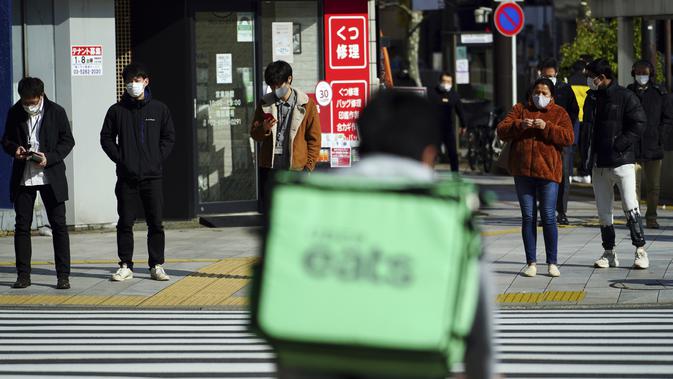 Orang-orang mengenakan masker untuk mencegah penyebaran virus corona menunggu lampu lalu lintas di persimpangan di Tokyo (8/2/2021). Ibukota Jepang mengonfirmasi lebih dari 270 kasus virus korona baru pada hari Senin. (AP Photo/Eugene Hoshiko)
