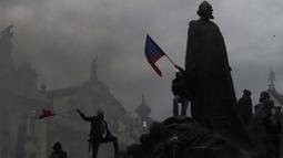 Demonstran memanjat monumen saat berkumpul untuk memprotes tindakan pembatasan COVID-19 di Old Town Square di Praha, Republik Ceko pada 18 Oktober 2020. Ceko  memberlakukan serangkaian tindakan pembatasan baru sebagai tanggapan atas rekor lonjakan infeksi virus corona. (AP Photo/Petr David Josek)