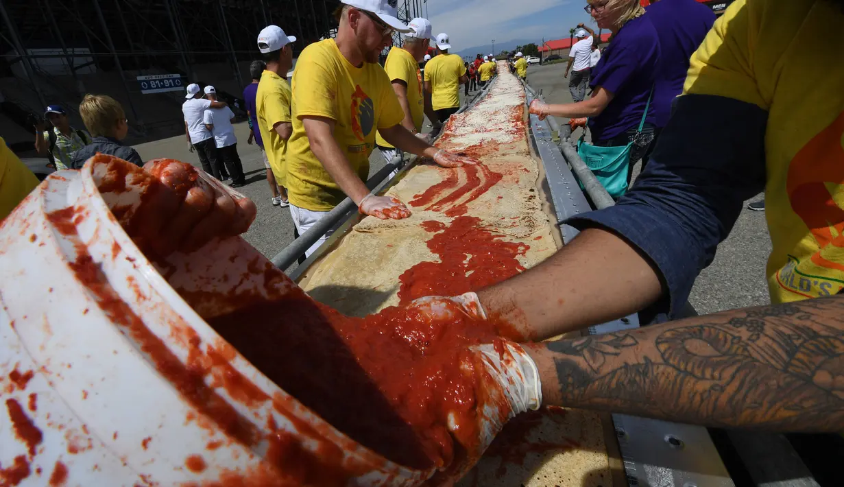 Sejumlah peserta menaburi saus tomat saat membuat pizza panjang di jalur Auto Club Speedway, di Fontana, California (10/6). Rekor baru ini mengalahkan rekor sebelumnya yang dipegang oleh peserta di Italia dengan pizza sepanjang 1,8 km. (AFP/Mark Ralston)