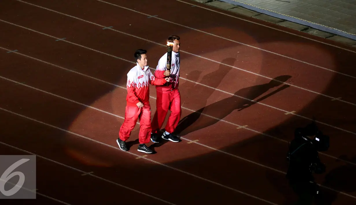Liliyana Natsir (kiri) dan Tontowi Ahmad berlari membawa obor api PON XIX Jabar saat upacara pembukaan di Stadion Gelora Bandung Lautan Api, Bandung, Sabtu (17/9). PON XIX Jabar berlangsung hingga 29 September. (Liputan6.com/Helmi Fithriansyah)