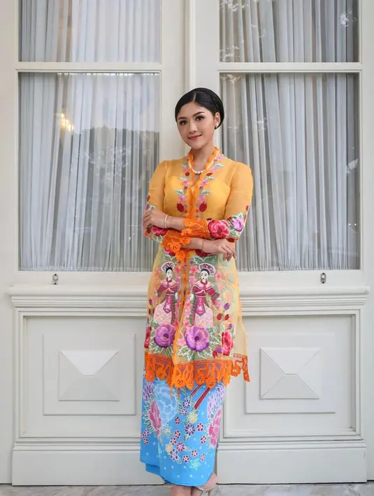 Erina Gudono tampil anggun dalam balutan kebaya encim berwarna oranye motif penari dipadu kain batik Betawi berwarna sky blue. Penampilannya dipermanis dengan anting dan kalung mutiara. [Instagram/erinagudono]