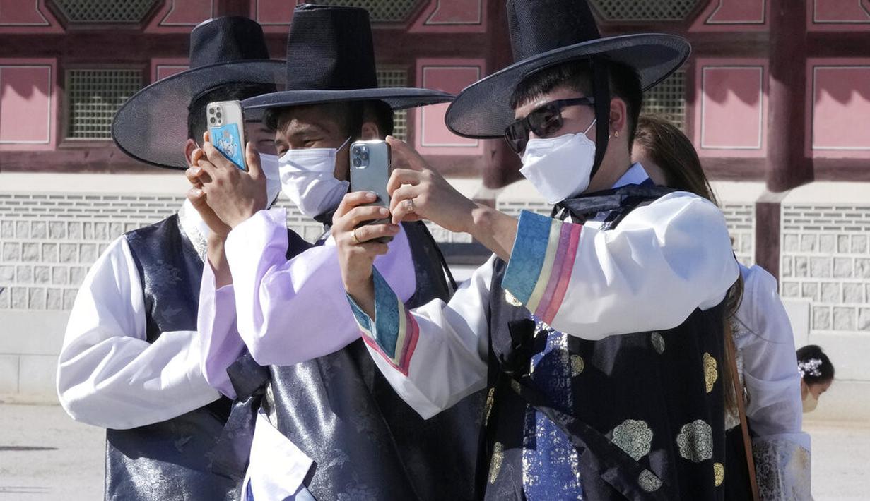 Para pria yang mengenakan masker sebagai tindakan pencegahan terhadap virus corona mengambil foto saat mereka berkunjung untuk merayakan liburan Chuseok, Hari Thanksgiving versi Korea, di Istana Gyeongbok di Seoul, Korea Selatan, Rabu (22/9/2021). ( AP Photo/Ahn Young-joon)