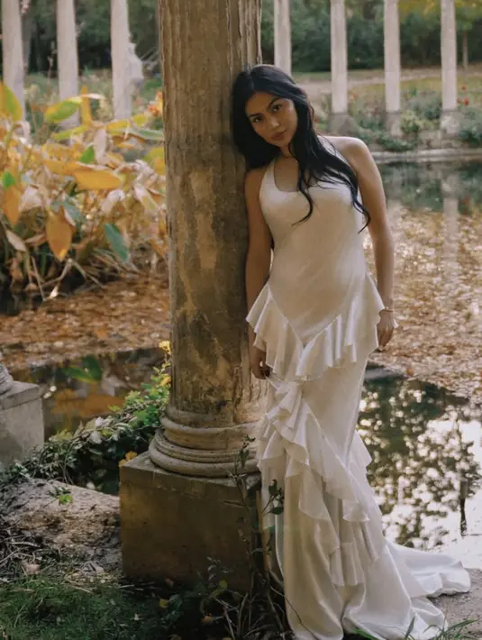 Gaun yang dikenakannya mengusung siluet feminin dengan potongan yang mengikuti lekuk tubuh. Detail ruffle bertumpuk di bagian bawah memberikan sentuhan dramatis sekaligus lembut, menciptakan efek flowy yang elegan saat dikenakan. [@npmalina]