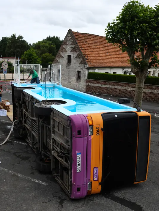 Seorang pria bekerja pada bus kota yang diubah menjadi kolam renang di Gosnay, Prancis Utara pada 15 Juli 2019. Seniman Prancis Benedetto Bufalino mengubah bangkai bus menjadi kolam renang yang bisa digunakan warga untuk berenang dan bersantai. (DENIS CHARLET / AFP)