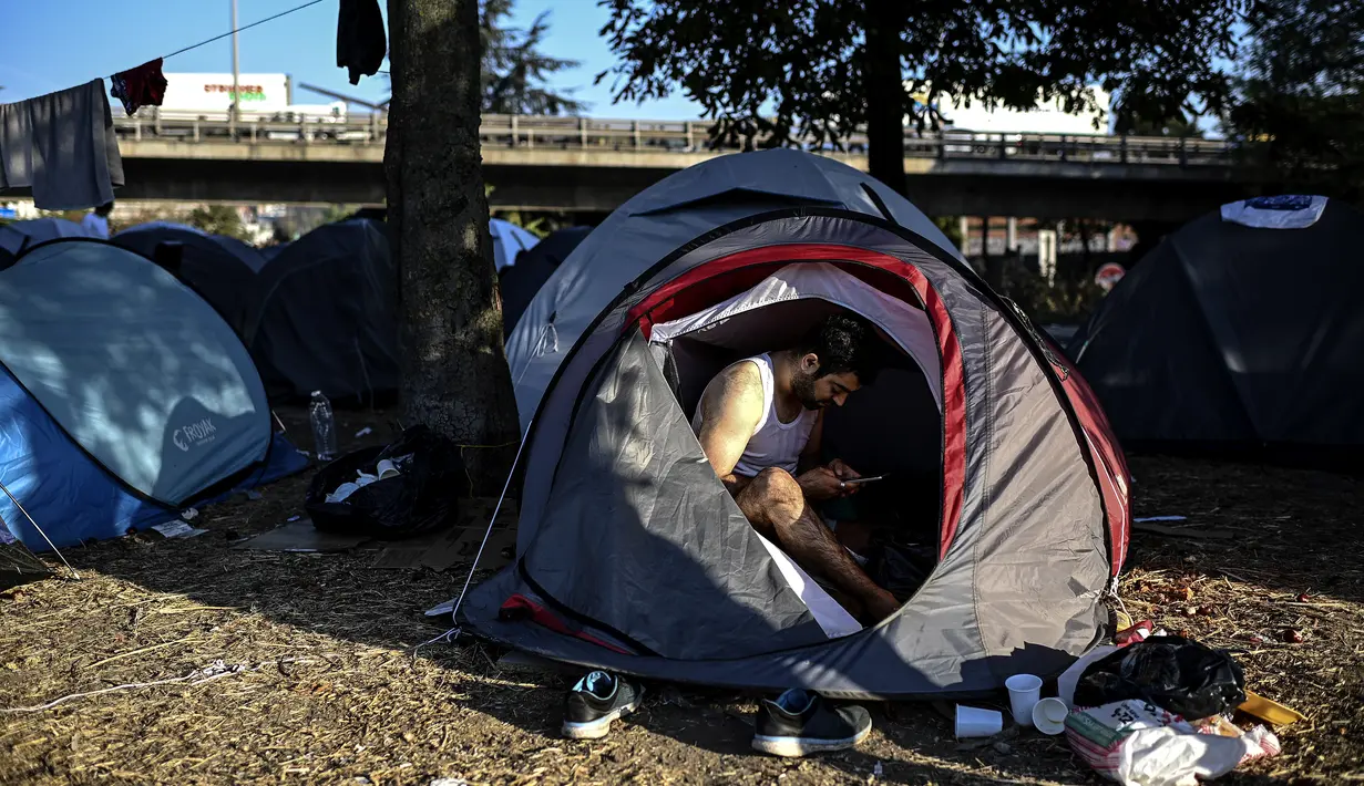 Seorang imigran Afghanistan sedang menggunakan ponselnya saat bertahan di sebuah kamp darurat di jalan raya A1 di utara pinggiran Kota Paris Saint-Denis (16/9/2020). (AFP/Christophe Archambault)
