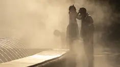 Seorang gadis kecil menyentuh kepala ayahnya saat mereka diselimuti kabut dari air mancur umum di Bukares, Rumania, Kamis (13/7/2023). (AP Photo/Andreea Alexandru)