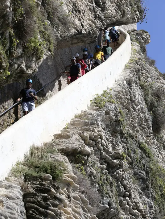 Turis menuruni tangga Raja Aragon di Bonifacio di pulau Corsica, Mediterania Prancis (19/9/2021). Menurut legendanya, Tangga Raja Aragon, sebuah monumen bersejarah Corsica, digali dengan tangan di tebing batu kapur di suatu malam oleh pasukan Raja Aragon tahun 1420. (AFP/Pascal Pochard-Casabianca)