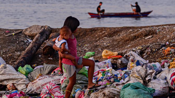 Seorang anak perempuan membawa adiknya berjalan di tumpukan sampah di permukiman kumuh di sepanjang garis Pantai Baseco di Manila (28/9/2019). Daerah memiliki pantai yang sering dikunjungi beberapa warga Manila meskipun tingkat coliform berbahaya di perairan yang berdekatan. (AFP Photo/Maria Tan)