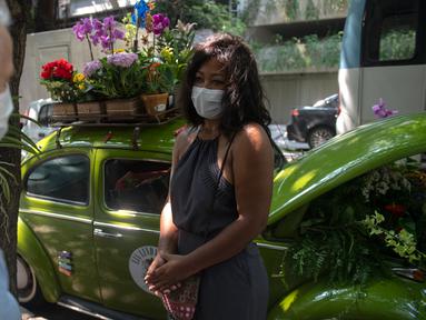 Roberta Machado (kanan) asal Brasil dan pelanggan berbincang di sebelah VW Beetle 1969 miliknya yang diubah menjadi toko bunga keliling di Copacabana, Rio de Janeiro, Rabu (14/10/2020). Perempuan 51 tahun ini mengubah VW kodok untuk bertahan dari krisis akibat pandemi COVID-19. (MAURO PIMENTEL/AFP)