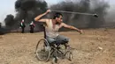 Seorang pria Palestina bernama Saber al-Ashkar melemparkan batu dari kursi rodanya saat terlibat bentrokan dengan pasukan Israel di jalur Gaza (11/5). Sejauh ini lebih dari 50 warga Palestina tewas oleh tembakan tentara Israel. (AFP/Mahmud Hams)