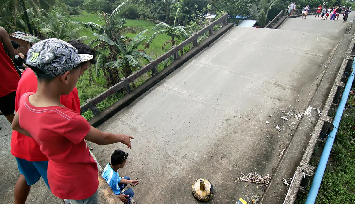 Sejumlah warga berdiri di salah satu ujung jembatan yang roboh akibat gempa 6,5 SR yang melanda Surigao City, Pulau Mindanao, Filipina (11/2). Setelah gempa itu usai, tak kurang dari 100 gempa susulan terjadi. (AFP/Erwin Mascarinas)