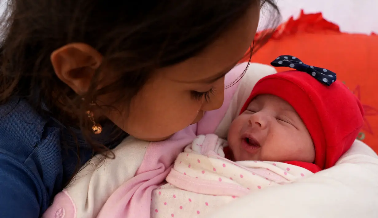 Seorang sepupu menggendong Afraa, bayi Suriah yang lahir di bawah reruntuhan setelah gempa bumi 6 Februari yang melanda Turki dan Suriah yang menewaskan orang tua dan saudara kandungnya, setelah dia diadopsi oleh keluarga pamannya, di kota Jindayris yang dikuasai pemberontak di Suriah utara, Selasa (21/2/2023). Staf medis melakukan tes DNA untuk memastikan mereka memang kerabat bayi tersebut dan akhirnya dijemput oleh paman serta bibinya setelah dokumen adopsinya selesai. (Rami al SAYED / AFP)