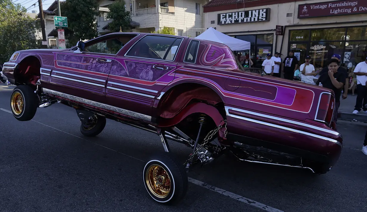 Sebuah mobil Lowrider melaju saat beratraksi dengan roda tiga di Sunset Boulevard, di lingkungan Echo Park, Los Angeles, pada 18 Juli 2021. Lowrider merupakan gaya dari kendaraan modifikasi yang bermula dari Los Angeles pada pertengahan hingga akhir 1940-an. (AP Photo/Damian Dovarganes)