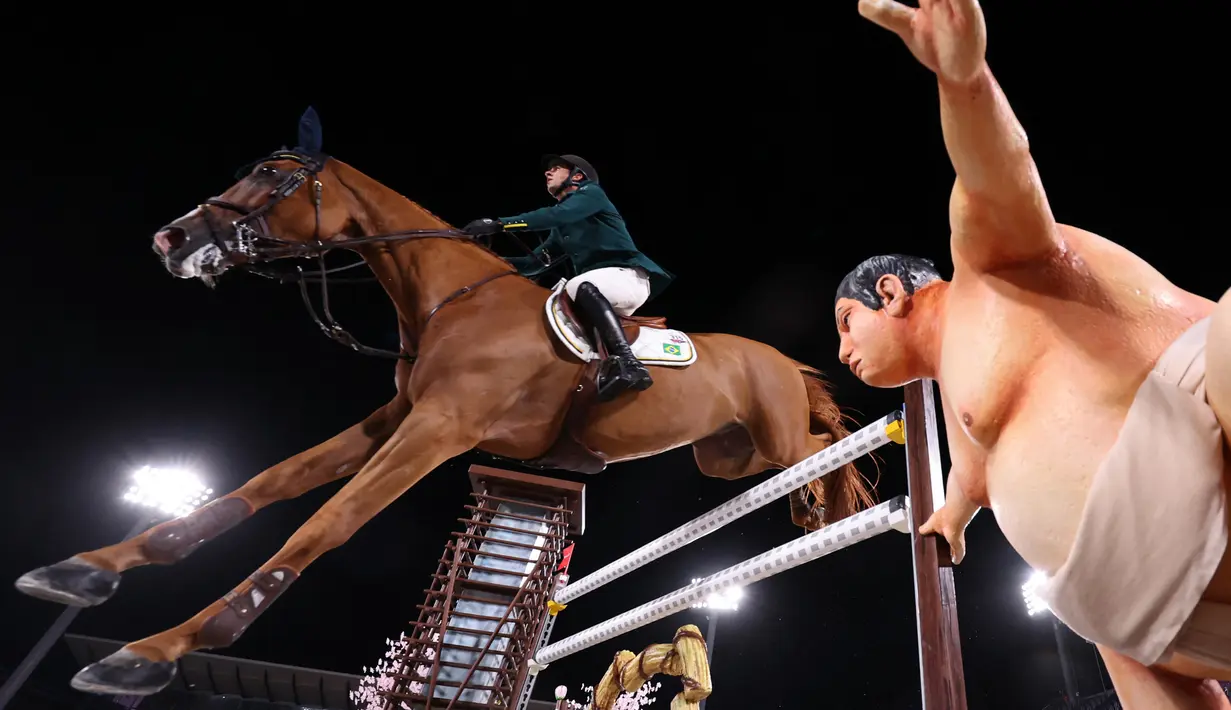 Marlon Modolo Zanotelli dari Brasil mengendarai Edgar M melewati patung pegulat sumo dalam kualifikasi individu lompat berkuda Olimpiade Tokyo 2020 di Equestrian Park di Tokyo (3/8/2021). Pihak panitia memasang patung simbol Jepang seperti sakura sampai pesumo di arena lintasan. (AFP/Behrouz Mehri)