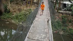 Seorang anak melintasi jembatan gantung semi permanen di kawasan Srengseng Sawah, Jakarta Selatan, Sabtu (24/8/2019). Jauhnya akses penyeberangan lain menyebabkan warga terpaksa memanfaatkan jembatan tersebut untuk menyeberangi Sungai Ciliwung. (Liputan6.com/Immanuel Antonius)