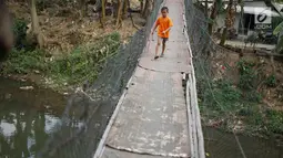 Seorang anak melintasi jembatan gantung semi permanen di kawasan Srengseng Sawah, Jakarta Selatan, Sabtu (24/8/2019). Jauhnya akses penyeberangan lain menyebabkan warga terpaksa memanfaatkan jembatan tersebut untuk menyeberangi Sungai Ciliwung. (Liputan6.com/Immanuel Antonius)