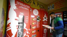 Seorang pria mengambil pesanannya di mesin penjual pizza otomatis, yang pertama dari jenisnya di pusat kota Roma, pada 29 April 2021. Mesin penjual otomatis ini mampu menguleni adonan, membumbui, memasak, dan menyajikan pizza dalam kotak karton hanya dalam waktu tiga menit. (Filippo MONTEFORTE/AFP)