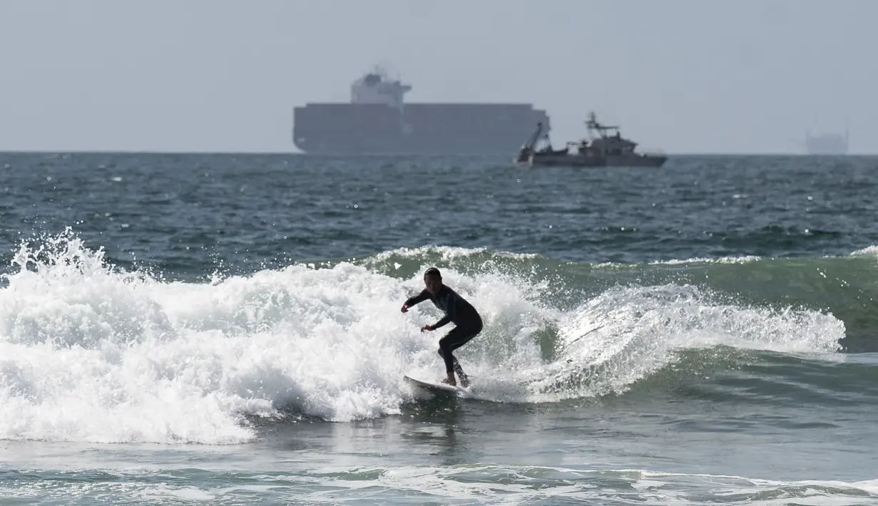 Peselancar melawan ombak di dekat dermaga di Huntington Beach, California (11/10/2021). Pantai Huntington membuka kembali garis pantainya setelah hasil pengujian air kembali dengan jumlah racun terkait minyak yang tidak terdeteksi di air laut. (Paul Bersebach/The Orange County Register via AP)