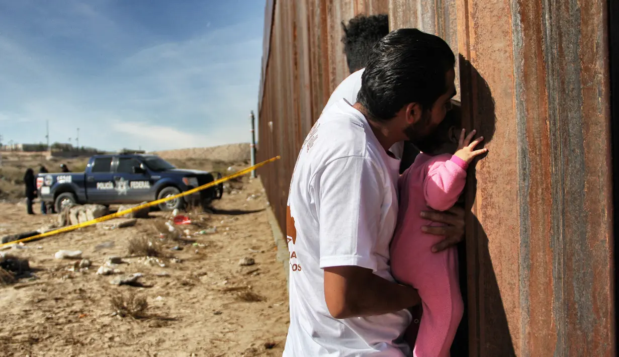 Seorang pria sambil menggendong bayi melepas rindu dengan kerabat dalam acara "Keep our dream alive" di dinding perbatasan antara Meksiko dan Amerika Serikat di Ciudad Juarez, negara bagian Chihuahua, 10 Desember 2017. (Herika MARTINEZ/AFP)