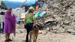 Seorang pria dan petugas penyelamat serta anjing pelacak berdiri di depan puing bangunan rumah yang rusak akibat gempa  6,2 SR di Amatrice, Italia tengah, Kamis (24/8). Sedikitnya enam orang tewas dalam bencana ini. (REUTERS/Emiliano Grillotti)