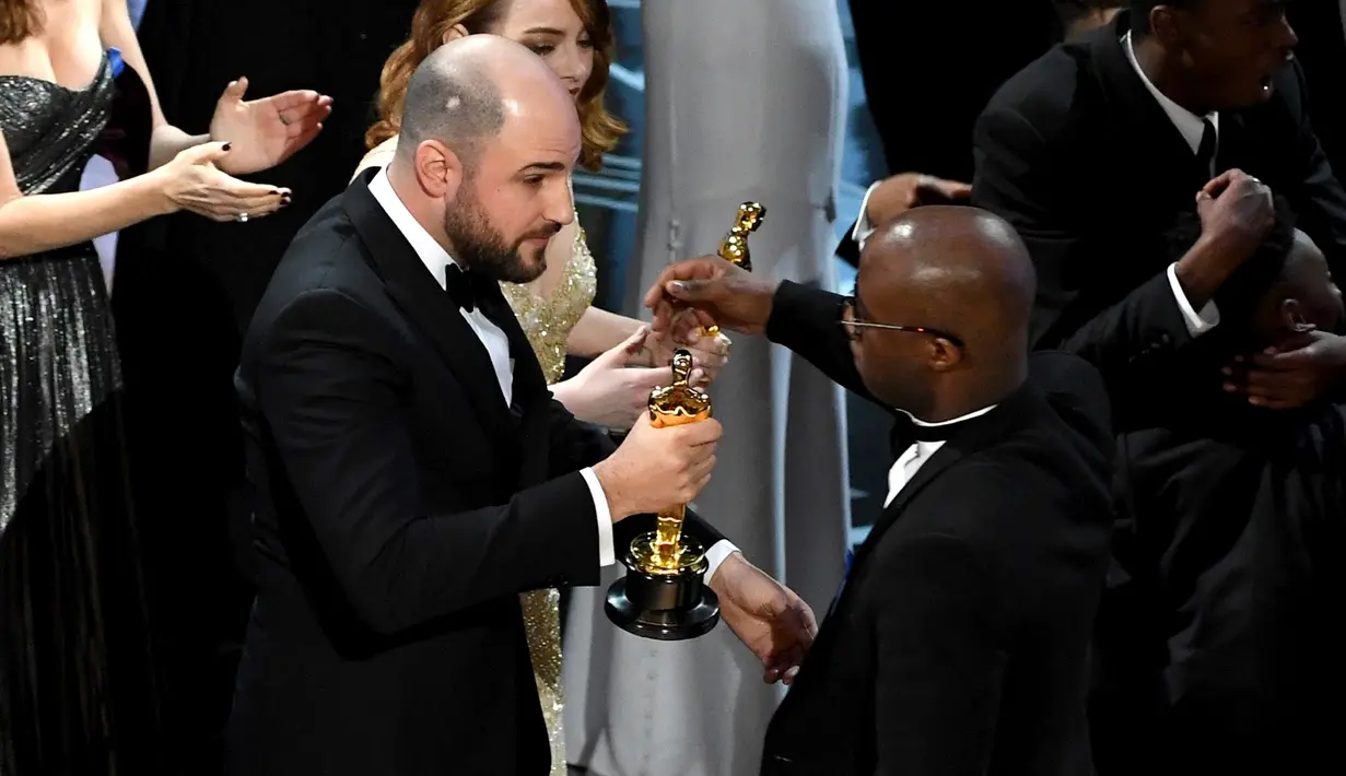 Produser La La Land, Jordan Horowitz (kiri) menyerahkan piala Oscar kepada sutradara Moonlight, Barry Jenkins usai kesalahan pembacaan pemenang film terbaik di ajang Oscar 2017 di Hollywood, California, AS (26/2). (AFP/ Getty Images/Kevin Winter)