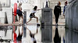 Pengunjung Albert Embankment di kaki Jembatan Westminster menghindari genangan air setelah hujan di London, 17 Agustus 2020. Cuaca hangat tampaknya telah menarik beberapa turis ke ibu kota meskipun tempat-tempat bersejarah masih jarang pengunjung, karena virus corona.  (Jonathan Brady/PA via AP)