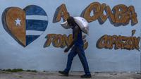 Seorang pekerja memuat sekarung beras untuk dikirim ke gudang negara di depan grafiti bertuliskan "Letakkan hati di Kuba" di Regla, Kuba, Senin, 1 Agustus 2022. Pengumuman pemadaman listrik muncul saat negara tersebut berjuang dengan krisis energi; banyak bagian negara telah mengalami pemadaman listrik setiap hari. (AP Photo/Ramon Espinosa)