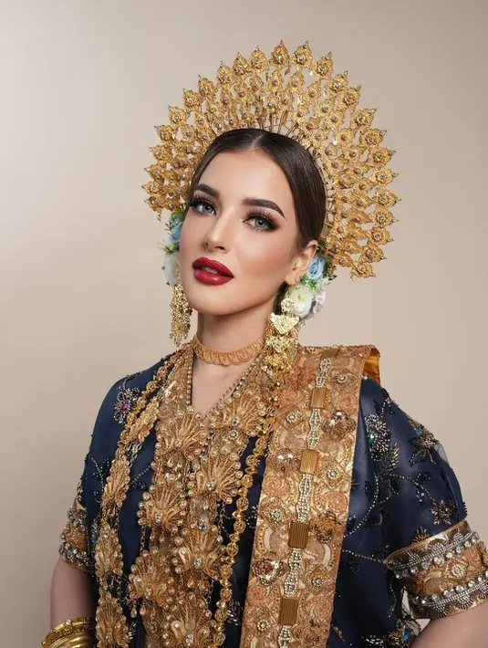 Sentuhan complexion flawless dengan contour tegas memberi dimensi pada wajahnya, sementara sapuan blush on peach merona menambahkan kesegaran yang kontras dengan busana serba keemasan.