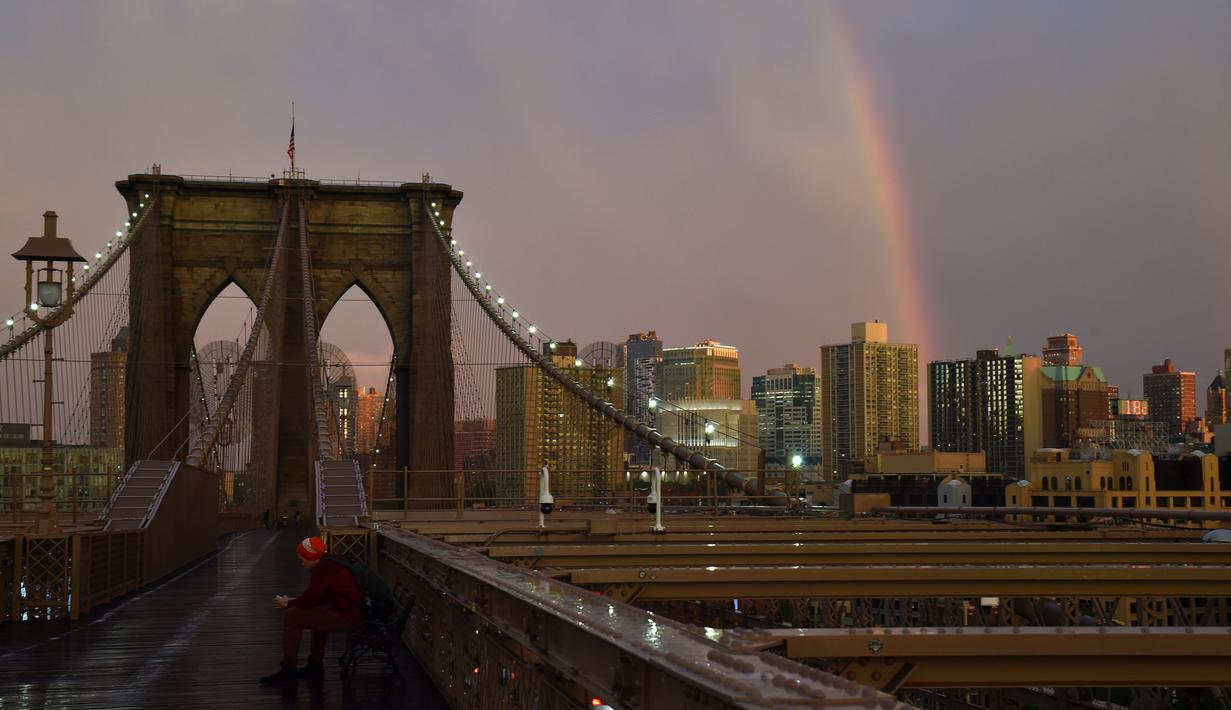 Warga beraktivitas saat pelangi terlihat dari Jembatan Brooklyn di New York City, AS (15/5). Jembatan ini selesai dibangun 1883 dan menghubungkan borough Manhattan dan Brooklyn di New York City melintasi Sungai East. (AFP Photo/Hector Retamal)