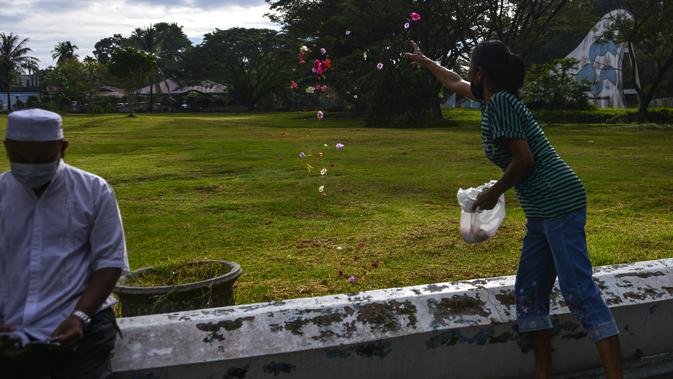 Seorang perempuan menaburkan kelopak bunga pada peringatan 16 tahun gempa bumi dan tsunami Aceh di sebuah kuburan massal di Siron, Sabtu (26/12/2020).  Peringatan di tengah pandemi COVID-19 itu tetap berlangsung secara sederhana melalui kegiatan ziarah kubur. (CHAIDEER MAHYUDDIN/AFP)