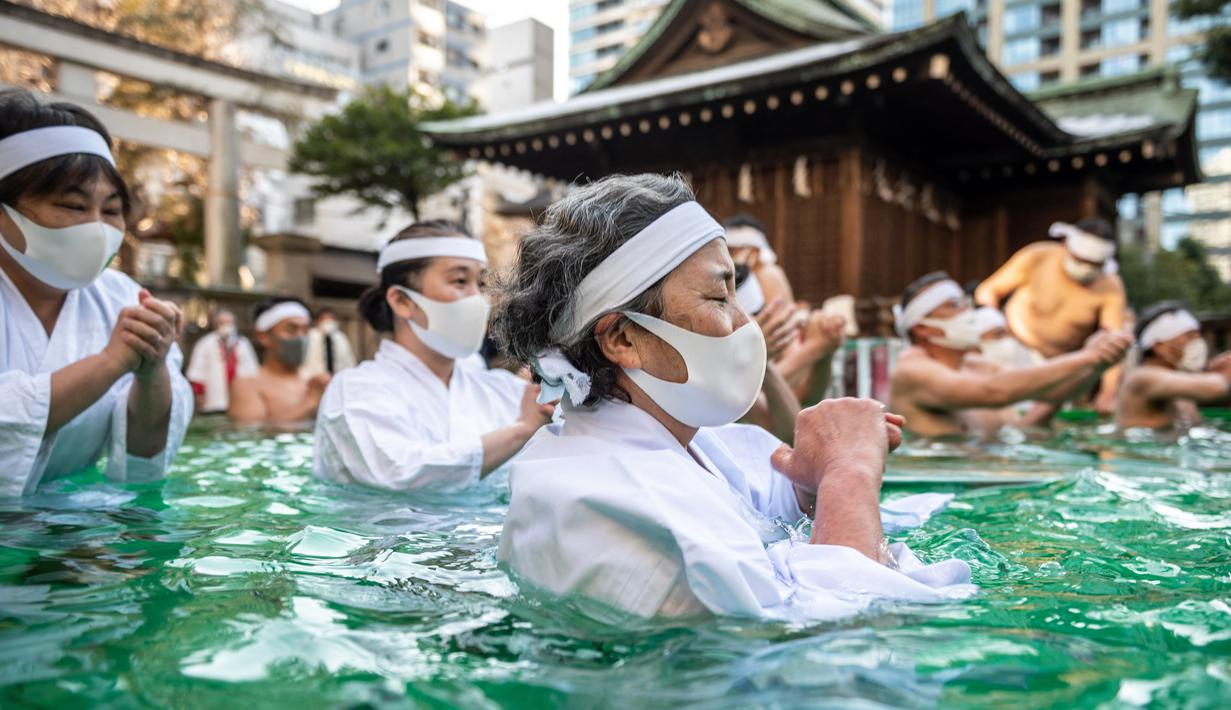 Penganut Shinto dari Kuil Teppozu Inari mandi dengan air dingin untuk mensucikan jiwa dan tubuh mereka selama ritual Tahun Baru di Tokyo, Jepang, Minggu (9/1/2022). Mereka melakukan prosesi mandi air dingin di sebuah bak yang telah disediakan oleh pihak kuil. (Philip FONG/AFP)