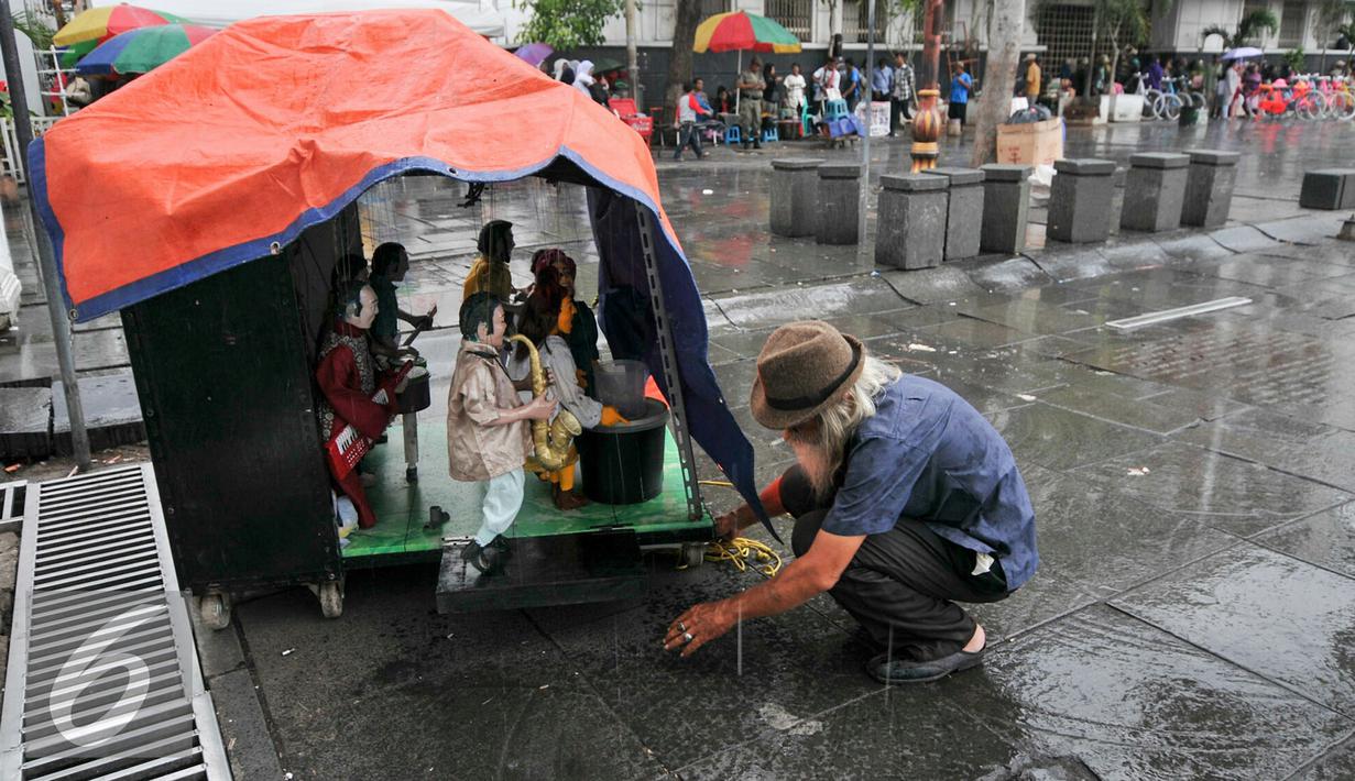 Seketika tetesan air hujan turun, tanda pertunjukan boneka kayu Muchtar harus terhenti, Jakarta, Kamis (17/12/2015). Dengan perlahan Muchtar menutup panggung boneka kayunya dengan sebuah terpal. (Liputan6.com/Yoppy Renato)