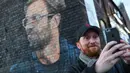 Seorang pria berswafoto dengan mural pelatih klub Liverpool, Jurgen Klopp di Baltic Triangle, Liverpool, Senin (10/12). Banyak yang menyambut pembuatan mural itu namun tidak sedikit pula yang mencibir, termasuk suporter klub Everton. (Paul ELLIS / AFP)
