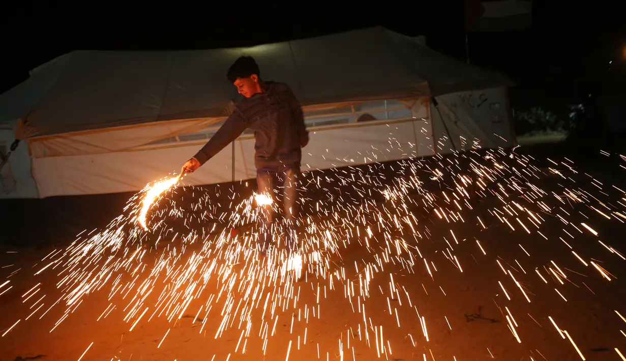 Seorang anak Palestina bermain kembang api di luar tenda di jalur perbatasan Gaza, Palestina (16/5). Mereka bermain kembang api untuk menyambut puasa pertama di bulan Ramadan. (AFP Photo/Said Khatib)
