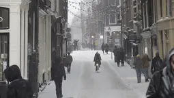 Seorang wanita mengendarai sepedanya di pusat kota Amsterdam, ketika salju dan angin kencang menyelimuti sebagian besar wilayah Belanda, Minggu (7/2/2021). Badai salju dengan suhu mencapai minus 10 derajat celsius membuat transportasi umum tidak beroperasi. (AP Photo/Peter Dejong)