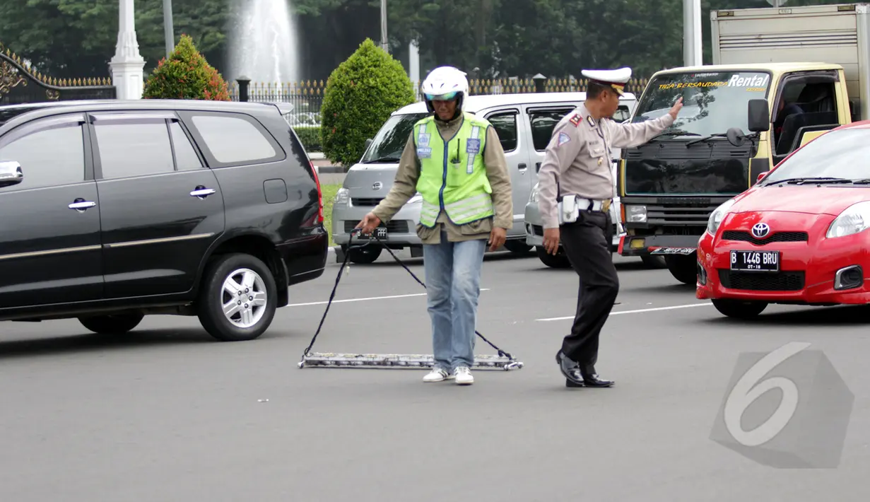 Petugas Polisi menertibkan jalan saat relawan Saber membersihkan ranjau paku di depan Istana Merdeka, Jakarta, Jumat (6/3/2015). Paku yang ditebar oleh orang tidak bertangung jawab seringkali mengganggu para pengguna jalan. (Liputan6.com/Faizal Fanani)