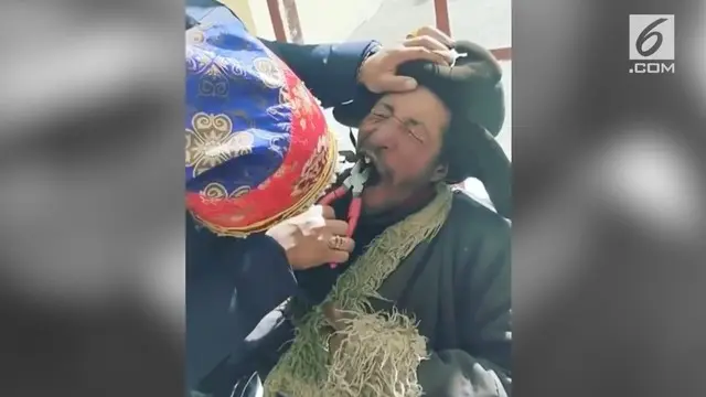 Seorang kakek memperlihatkan cara dirinya mencabut gigi memakain tang.