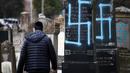 Seorang pria berjalan melewati makam Yahudi yang dicoret simbol Nazi di pemakaman Yahudi, Quatzenheim, Prancis, Selasa (19/2). Aksi vandalisme ini dilakukan terhadap sekitar 80 makam. (Frederick FLORIN/AFP)